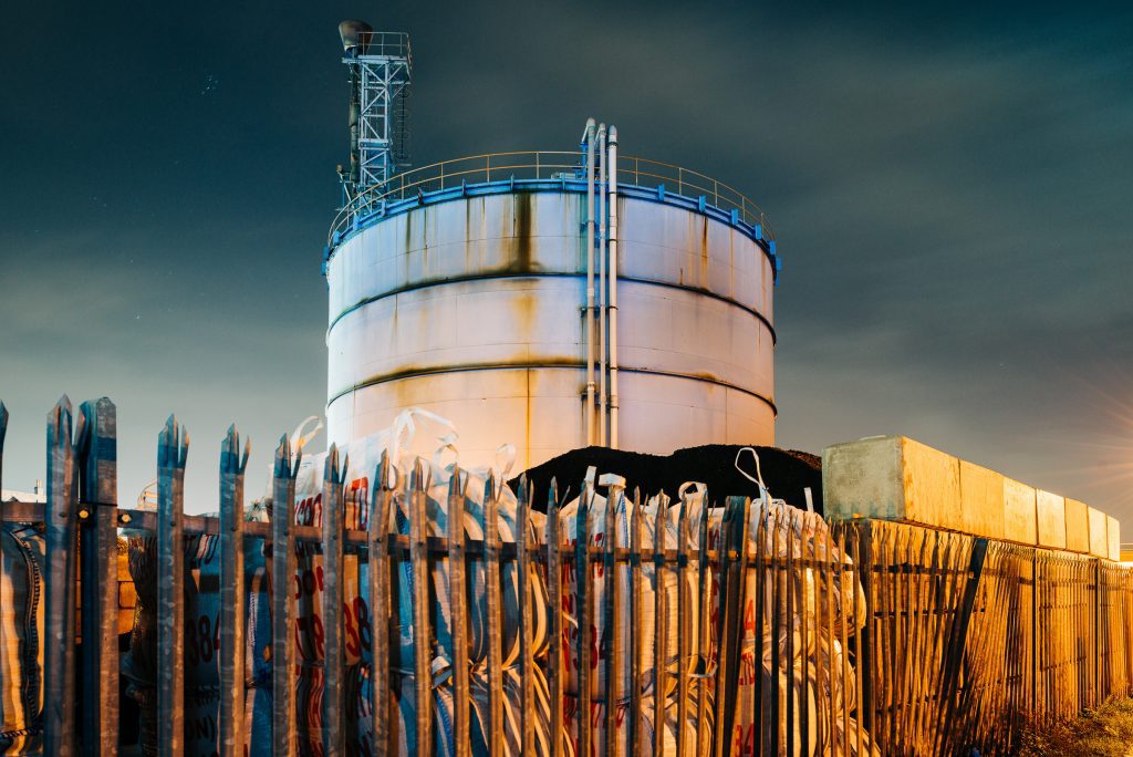 Gas storage tank with rusted chain-link fence at golden hour, Blackwall Tunnel, East London
