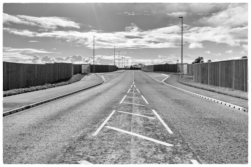 Empty road with geometric metal fencing and surveillance lighting, South Wales industrial estate