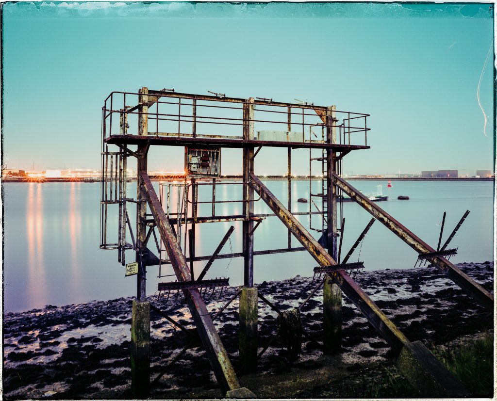 Derelict coal terminal gantry on the Thames foreshore near Woolwich during twilight.
